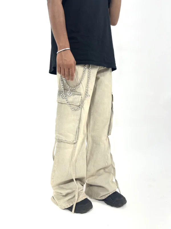 Sand color wide-leg cargo pants with washed finish, relaxed fit, and chain detail styled in a modern streetwear look.